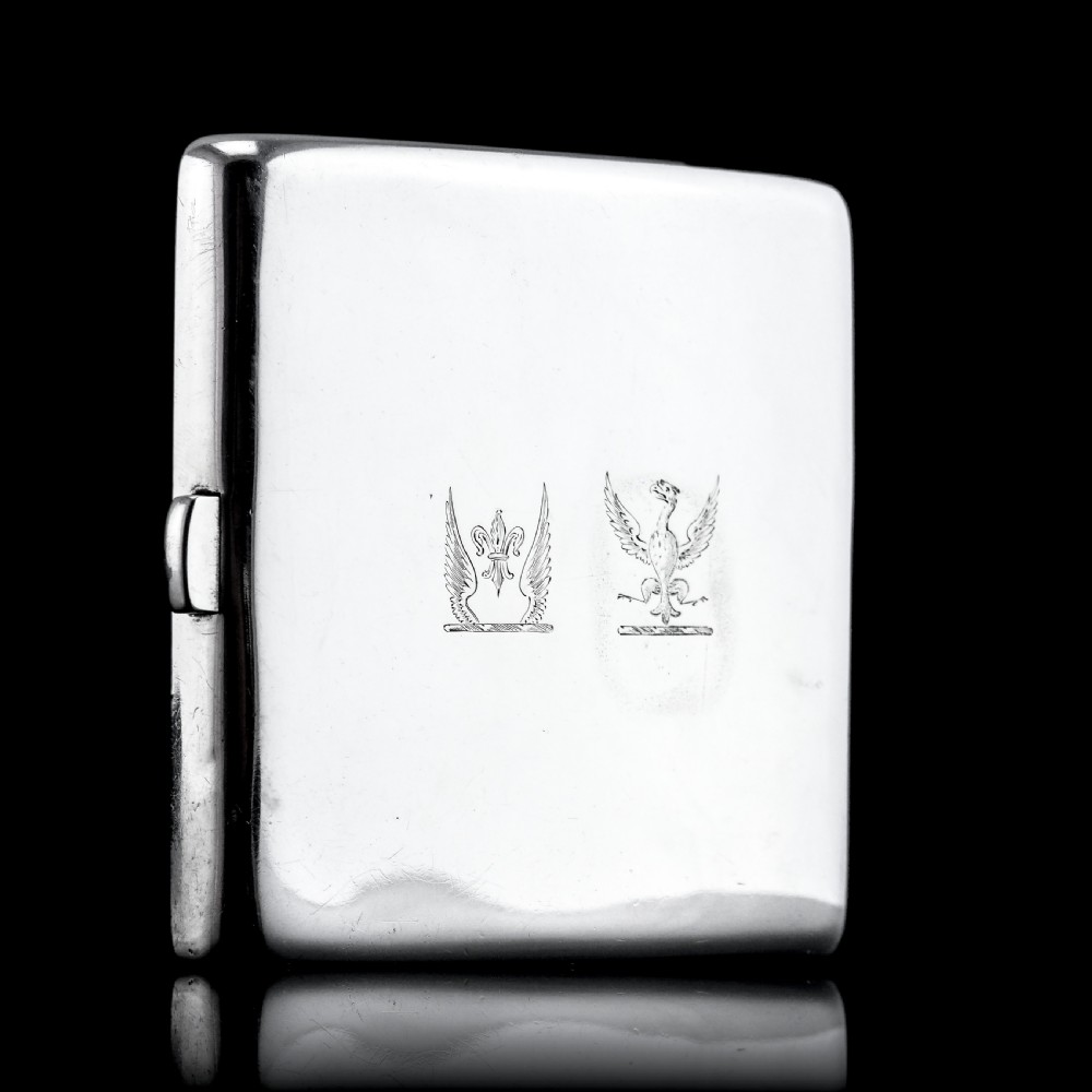 A polished Victorian sterling silver cigarette case featuring an engraved heraldic crest and curved profile resting on an open book. View XX