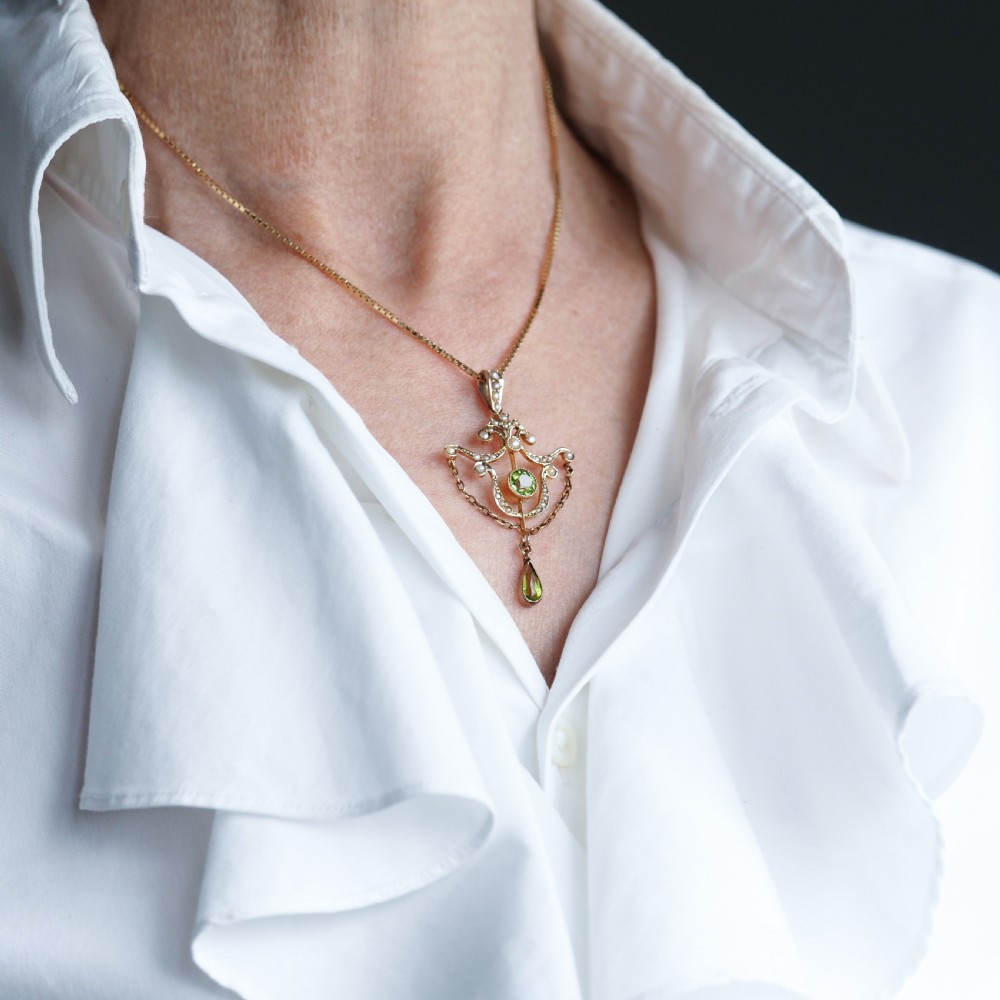 An Edwardian 9ct gold openwork pendant set with seed pearls, a central round peridot, and a dangling teardrop peridot. View X