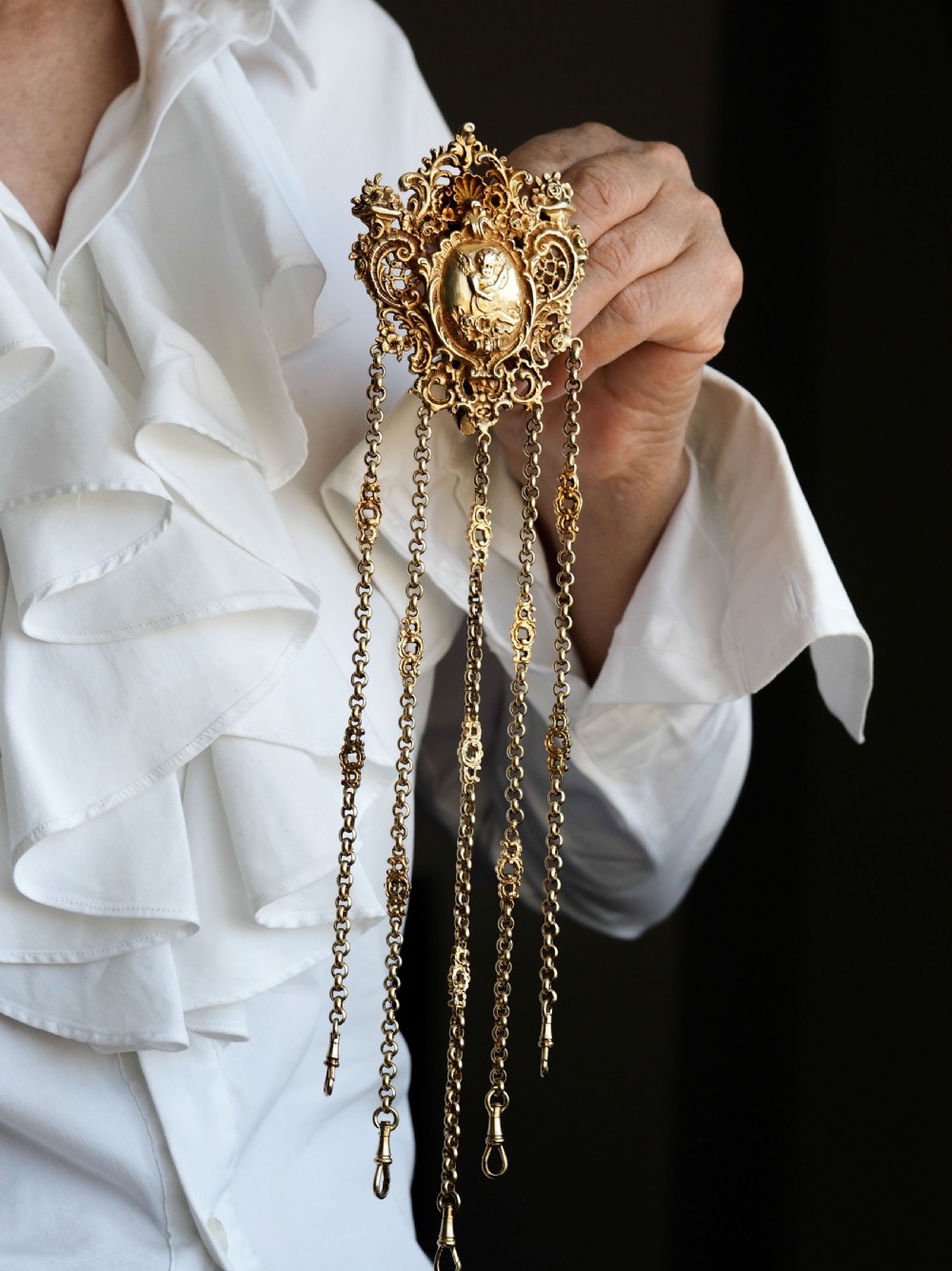 An ornate Victorian silver-gilt chatelaine featuring five hanging chains with swivel clips and a rococo plaque detailed with a central cherub motif. View VI
