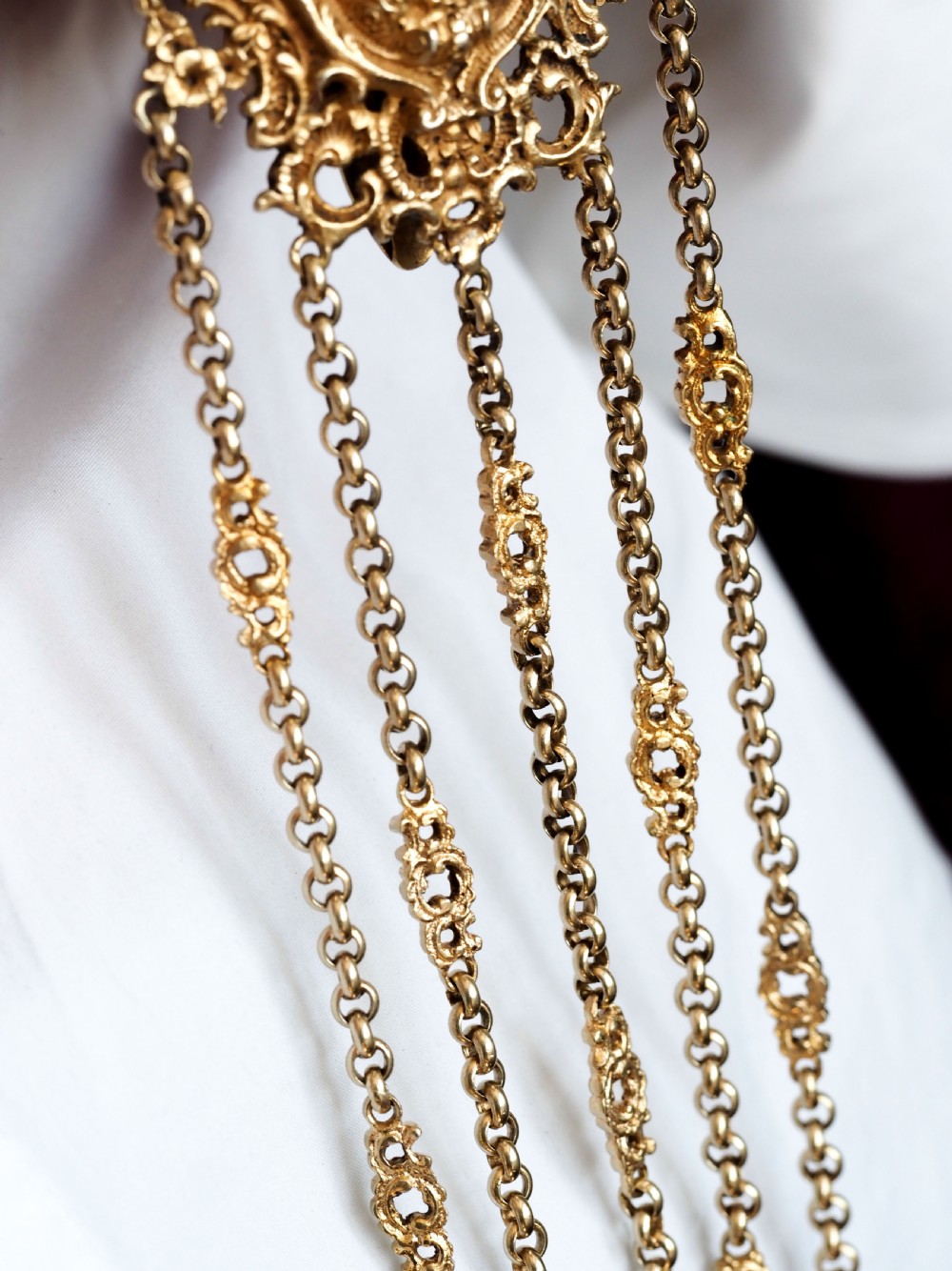 An ornate Victorian silver-gilt chatelaine featuring five hanging chains with swivel clips and a rococo plaque detailed with a central cherub motif. View IX