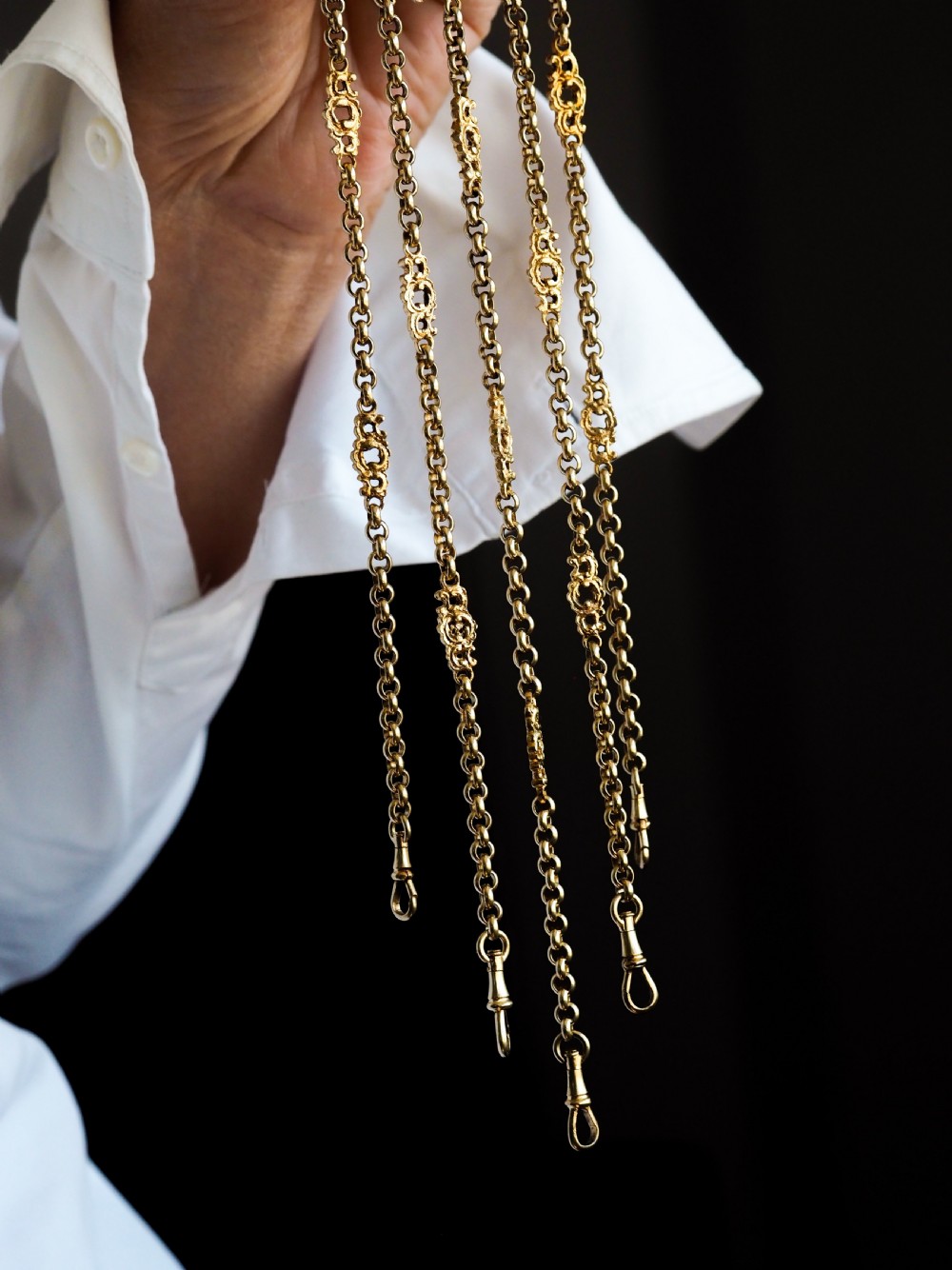 An ornate Victorian silver-gilt chatelaine featuring five hanging chains with swivel clips and a rococo plaque detailed with a central cherub motif. View X