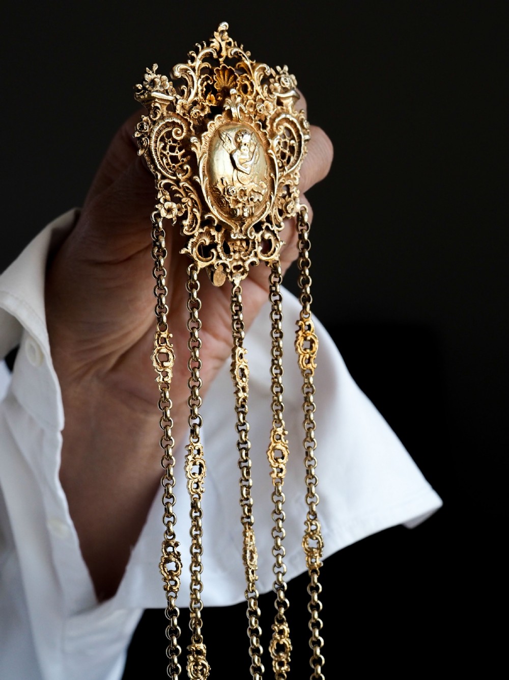 An ornate Victorian silver-gilt chatelaine featuring five hanging chains with swivel clips and a rococo plaque detailed with a central cherub motif. View XI