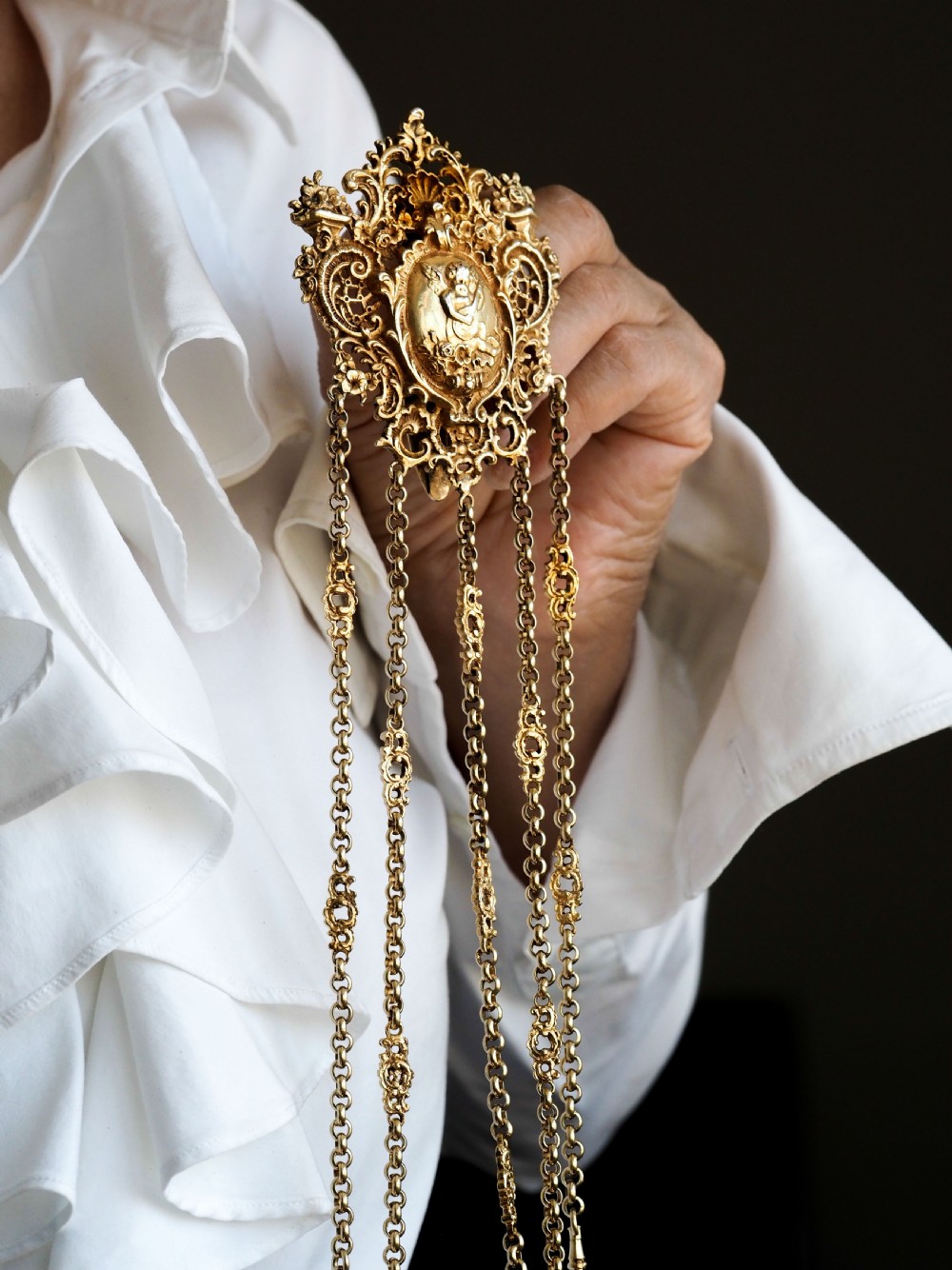 An ornate Victorian silver-gilt chatelaine featuring five hanging chains with swivel clips and a rococo plaque detailed with a central cherub motif. View XII
