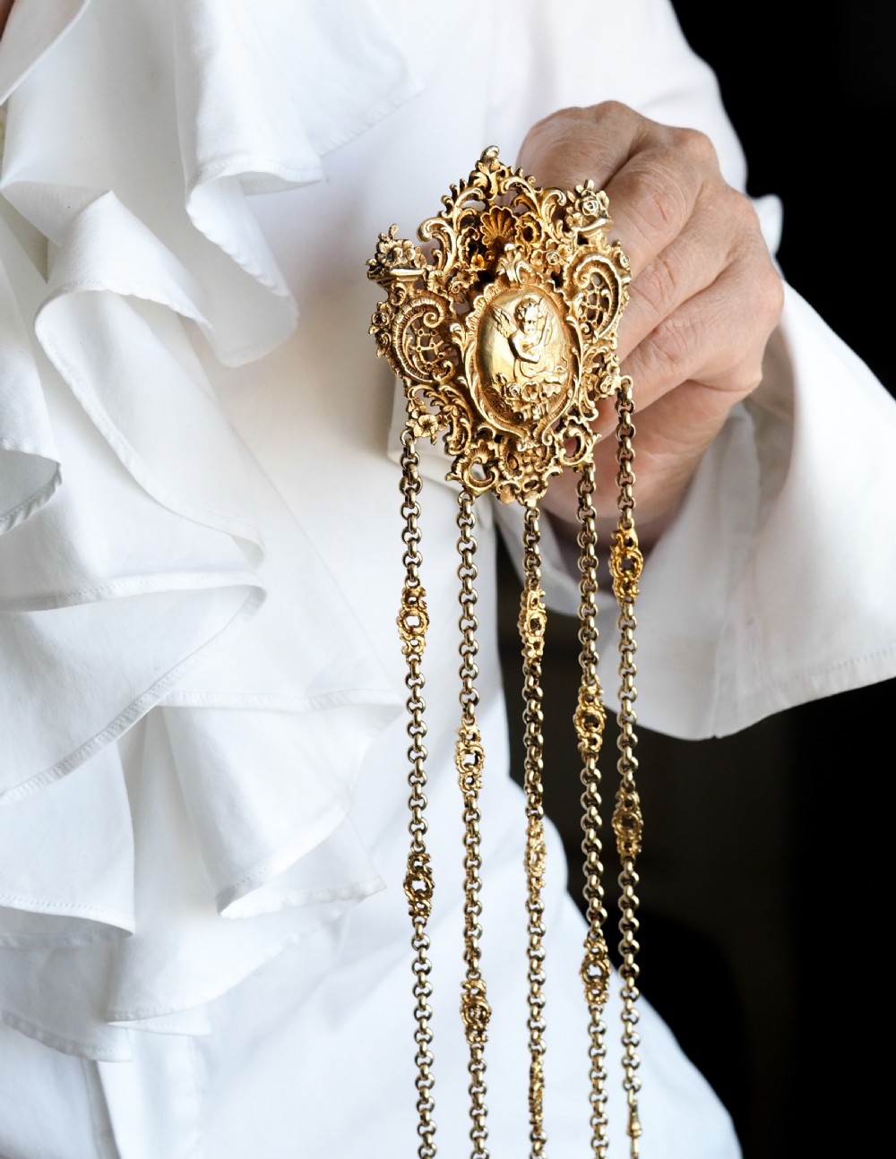 An ornate Victorian silver-gilt chatelaine featuring five hanging chains with swivel clips and a rococo plaque detailed with a central cherub motif. View XIV