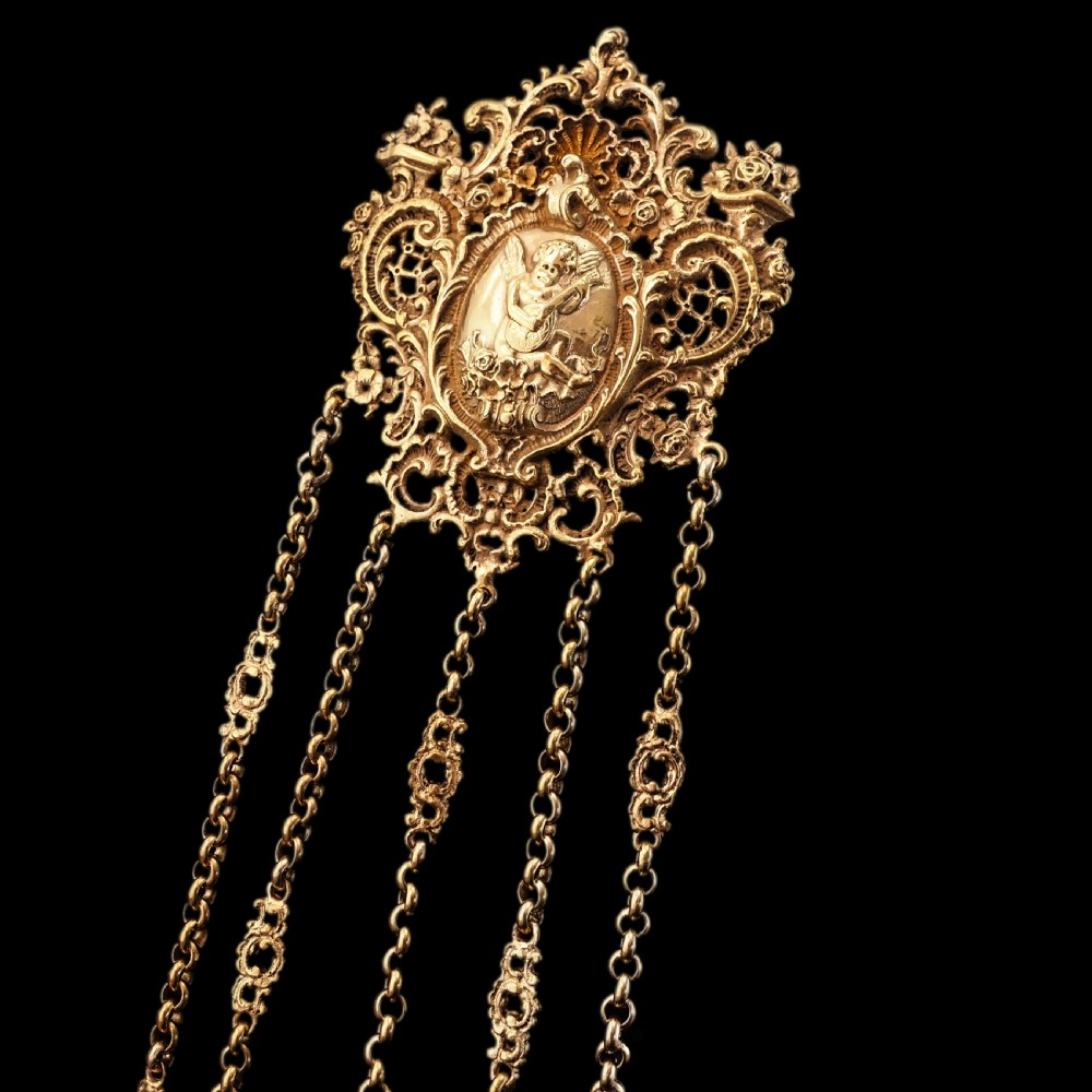 An ornate Victorian silver-gilt chatelaine featuring five hanging chains with swivel clips and a rococo plaque detailed with a central cherub motif. View XV
