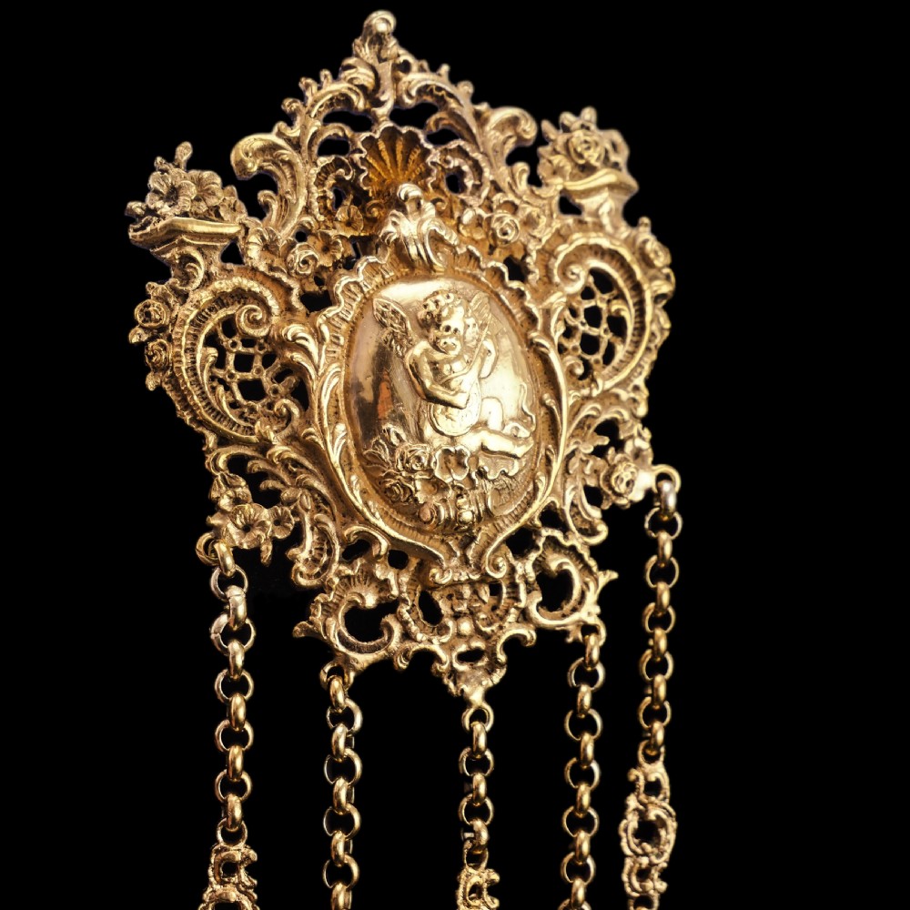 An ornate Victorian silver-gilt chatelaine featuring five hanging chains with swivel clips and a rococo plaque detailed with a central cherub motif. View XVI