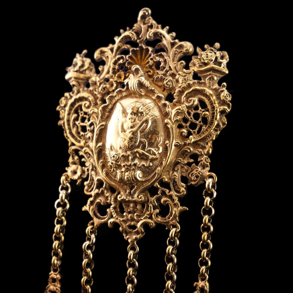 An ornate Victorian silver-gilt chatelaine featuring five hanging chains with swivel clips and a rococo plaque detailed with a central cherub motif. View XVII