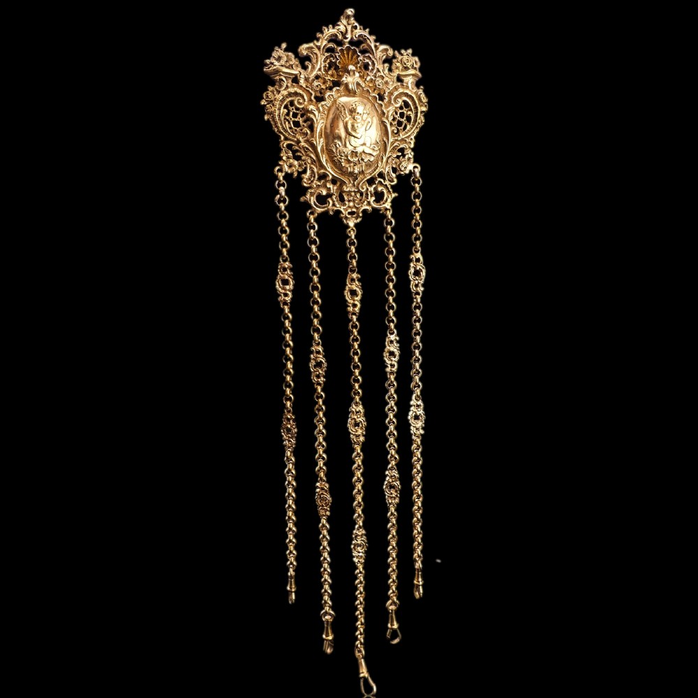 An ornate Victorian silver-gilt chatelaine featuring five hanging chains with swivel clips and a rococo plaque detailed with a central cherub motif. View XXIV