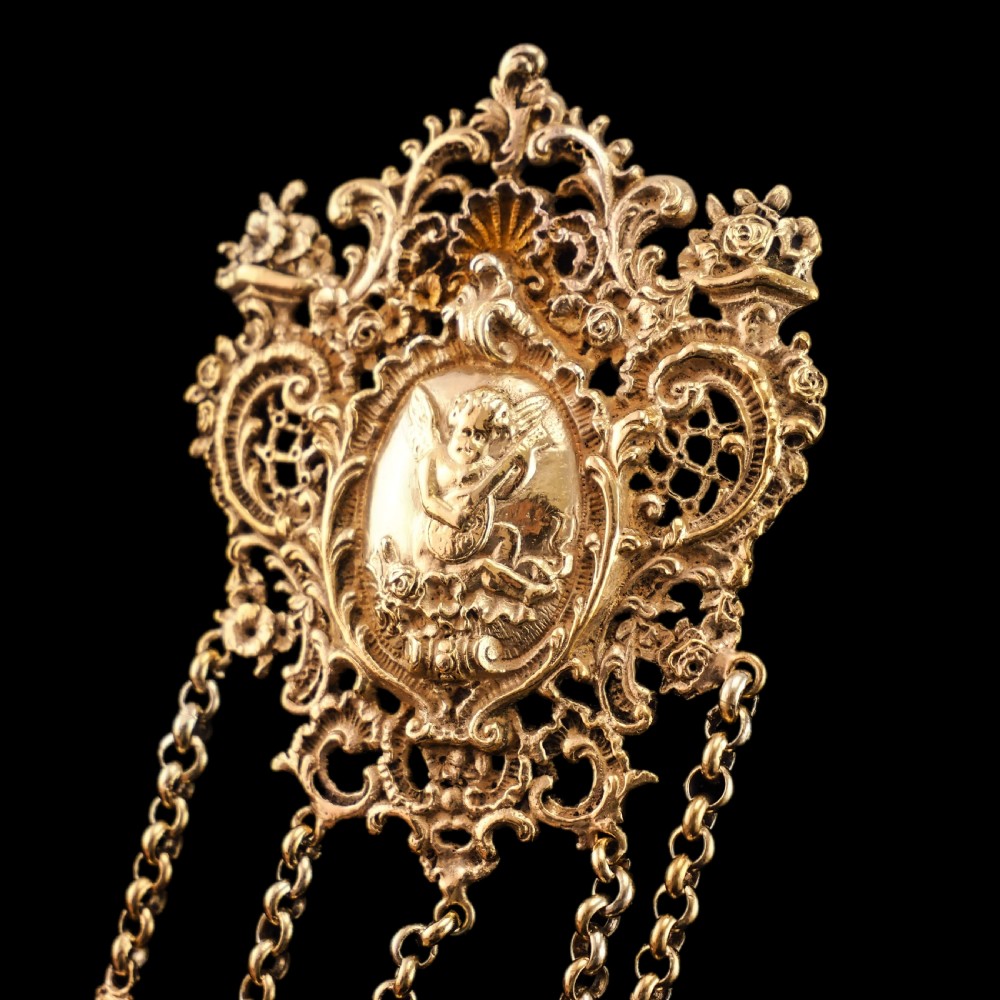 An ornate Victorian silver-gilt chatelaine featuring five hanging chains with swivel clips and a rococo plaque detailed with a central cherub motif. View XXV