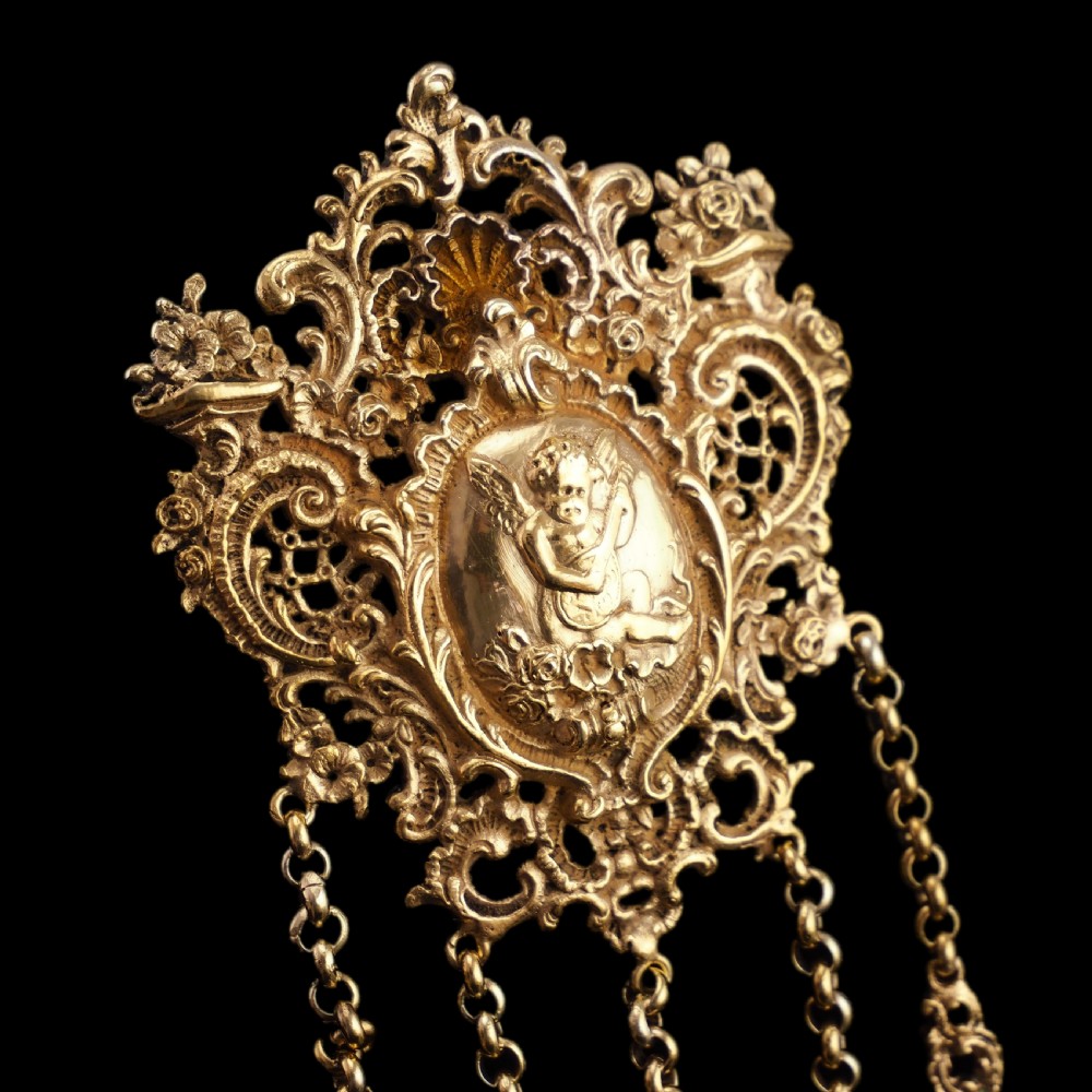 An ornate Victorian silver-gilt chatelaine featuring five hanging chains with swivel clips and a rococo plaque detailed with a central cherub motif. View XXVI