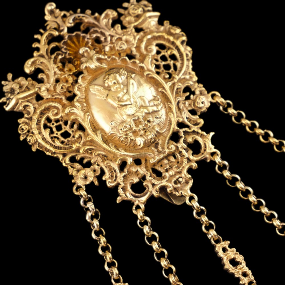 An ornate Victorian silver-gilt chatelaine featuring five hanging chains with swivel clips and a rococo plaque detailed with a central cherub motif. View XXVII