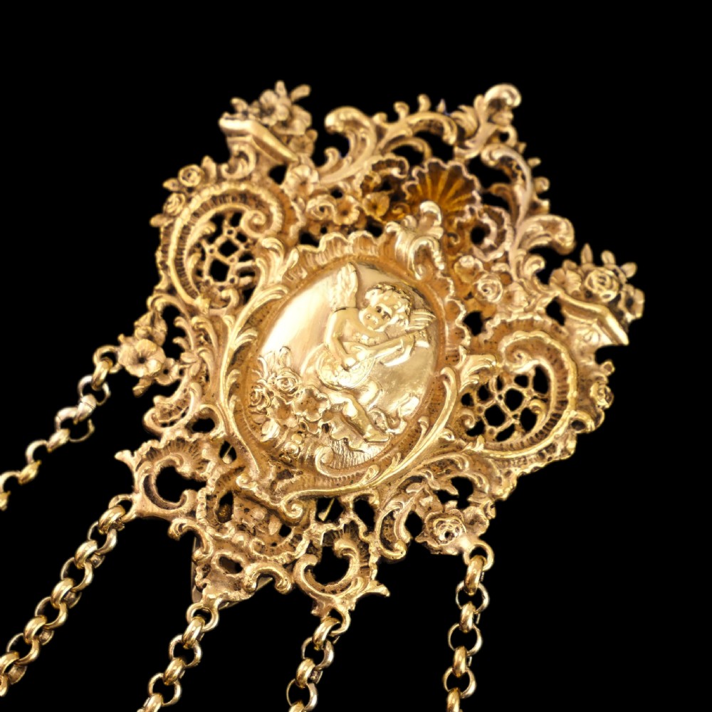 An ornate Victorian silver-gilt chatelaine featuring five hanging chains with swivel clips and a rococo plaque detailed with a central cherub motif. View XXVIII