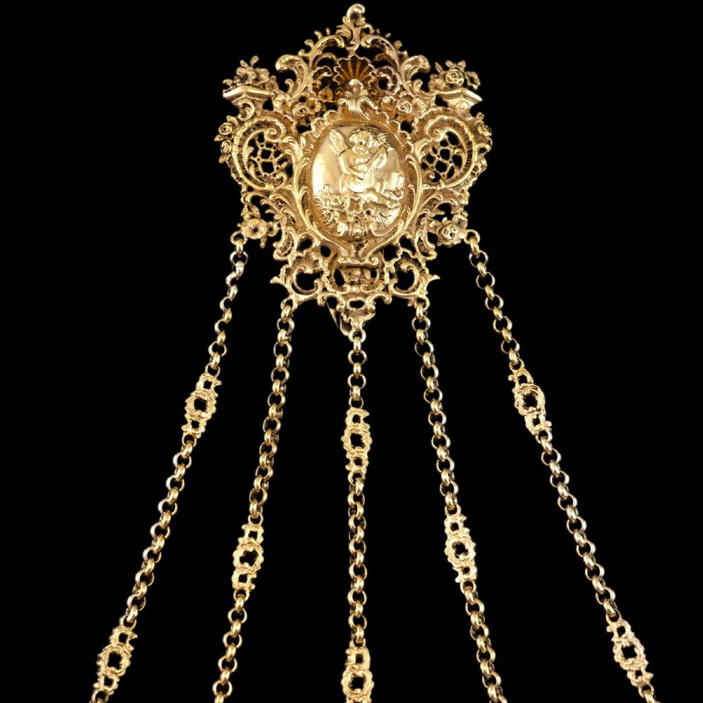 An ornate Victorian silver-gilt chatelaine featuring five hanging chains with swivel clips and a rococo plaque detailed with a central cherub motif. View XXIX