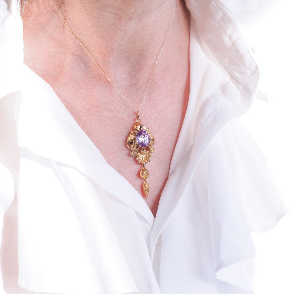 An antique 14ct yellow gold Victorian pendant featuring a central oval faceted amethyst surrounded by scrollwork, a shell motif, and an articulated drop element. View V