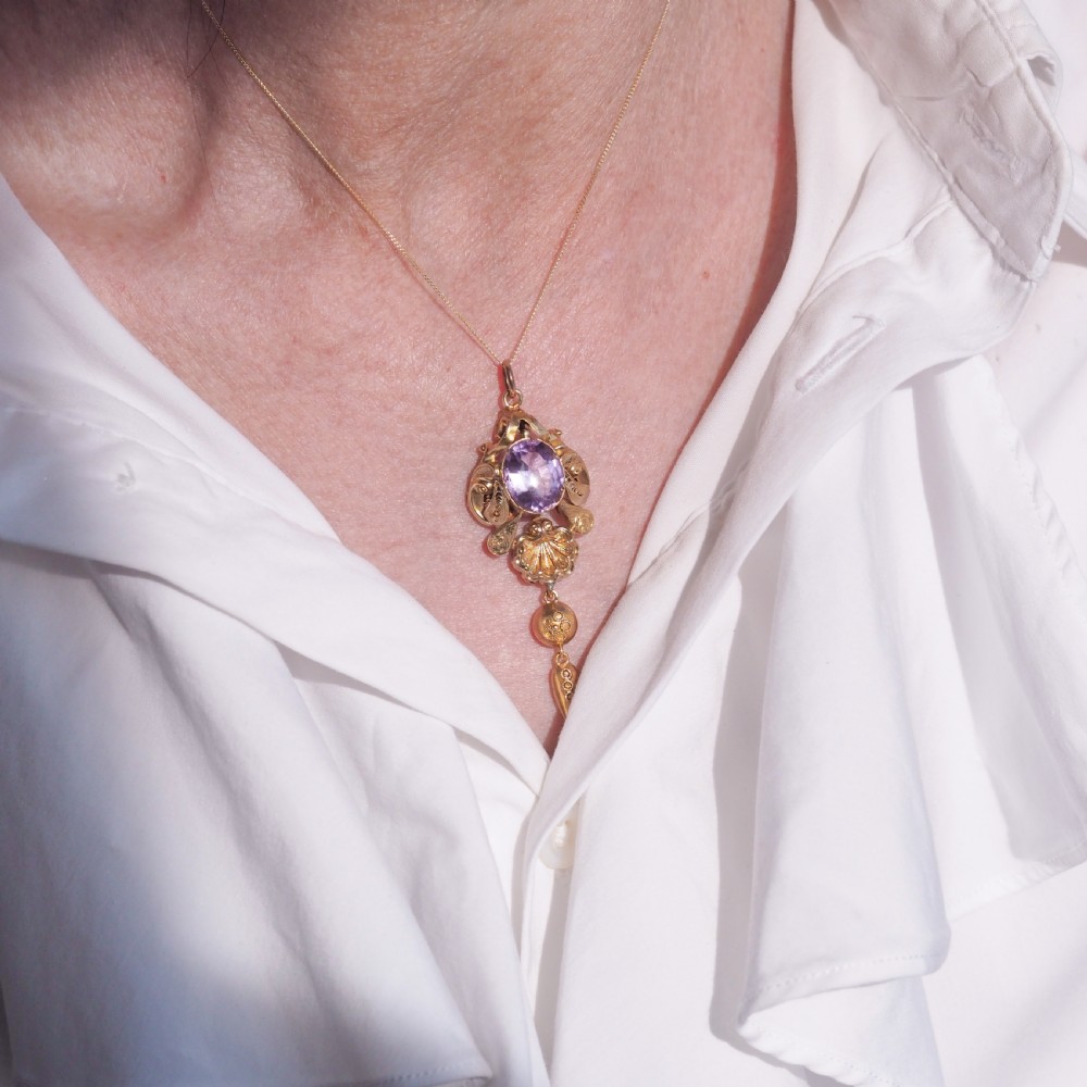An antique 14ct yellow gold Victorian pendant featuring a central oval faceted amethyst surrounded by scrollwork, a shell motif, and an articulated drop element. View VI