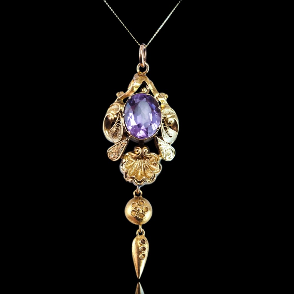 An antique 14ct yellow gold Victorian pendant featuring a central oval faceted amethyst surrounded by scrollwork, a shell motif, and an articulated drop element. View IX