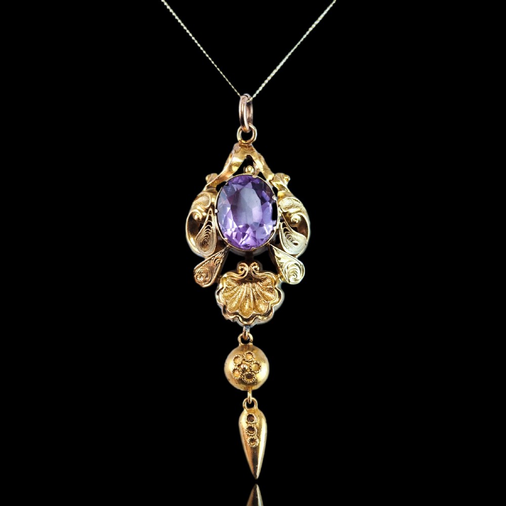 An antique 14ct yellow gold Victorian pendant featuring a central oval faceted amethyst surrounded by scrollwork, a shell motif, and an articulated drop element. View X