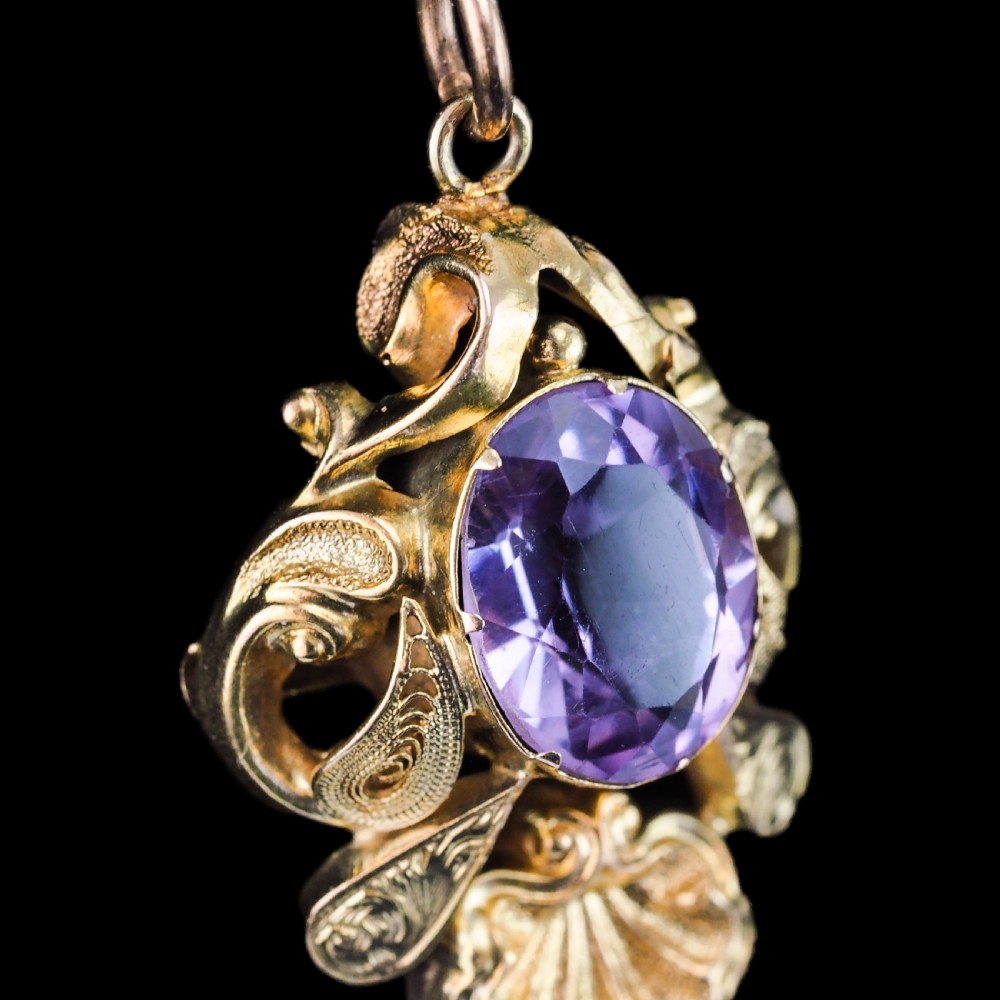 An antique 14ct yellow gold Victorian pendant featuring a central oval faceted amethyst surrounded by scrollwork, a shell motif, and an articulated drop element. View XIV