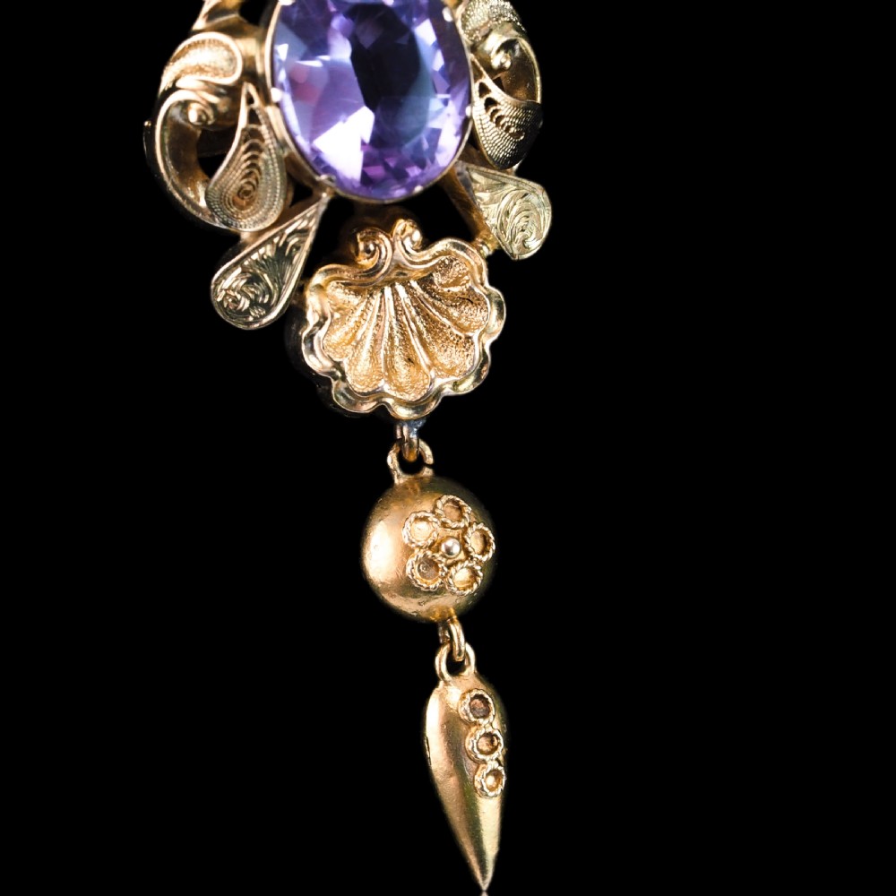An antique 14ct yellow gold Victorian pendant featuring a central oval faceted amethyst surrounded by scrollwork, a shell motif, and an articulated drop element. View XV