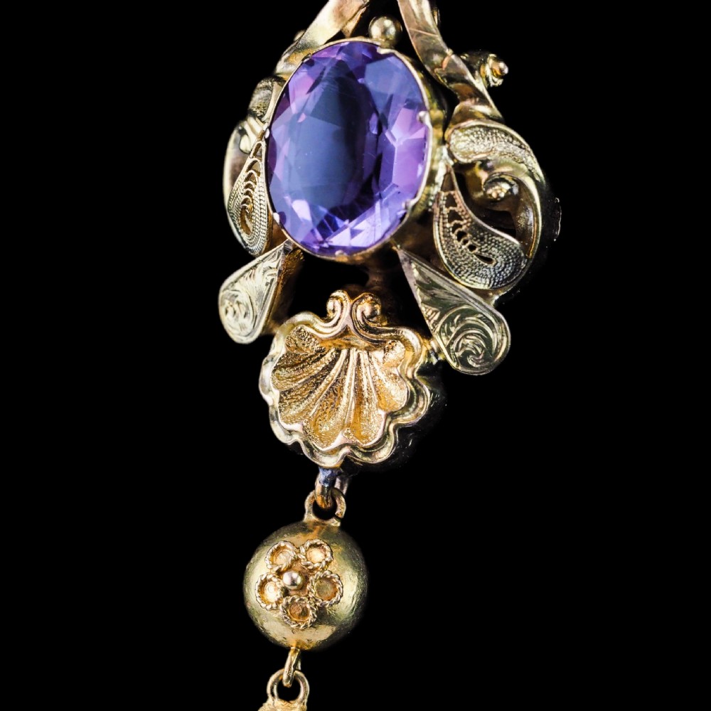 An antique 14ct yellow gold Victorian pendant featuring a central oval faceted amethyst surrounded by scrollwork, a shell motif, and an articulated drop element. View XVII