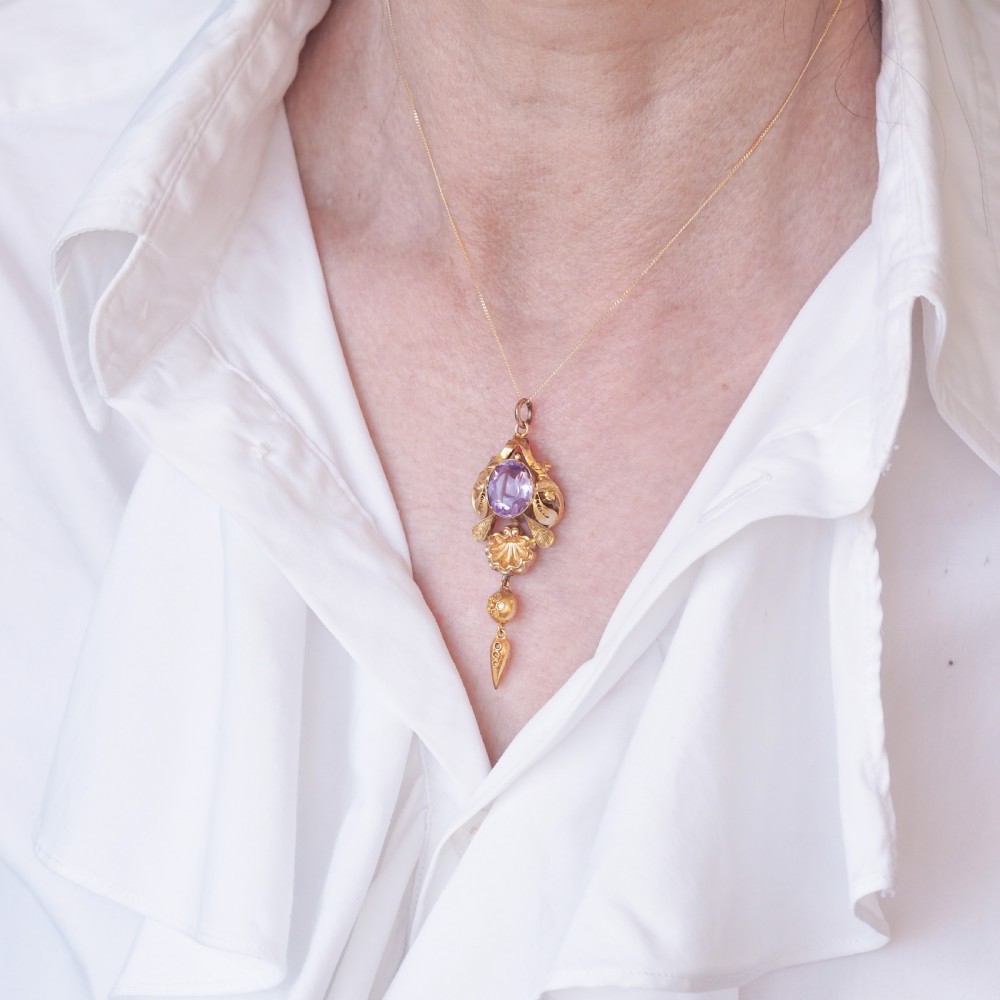 An antique 14ct yellow gold Victorian pendant featuring a central oval faceted amethyst surrounded by scrollwork, a shell motif, and an articulated drop element. View XVIII