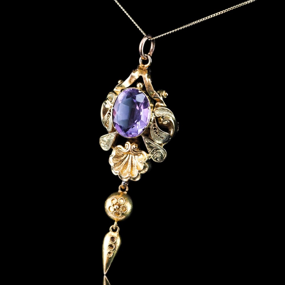 An antique 14ct yellow gold Victorian pendant featuring a central oval faceted amethyst surrounded by scrollwork, a shell motif, and an articulated drop element. View XIX