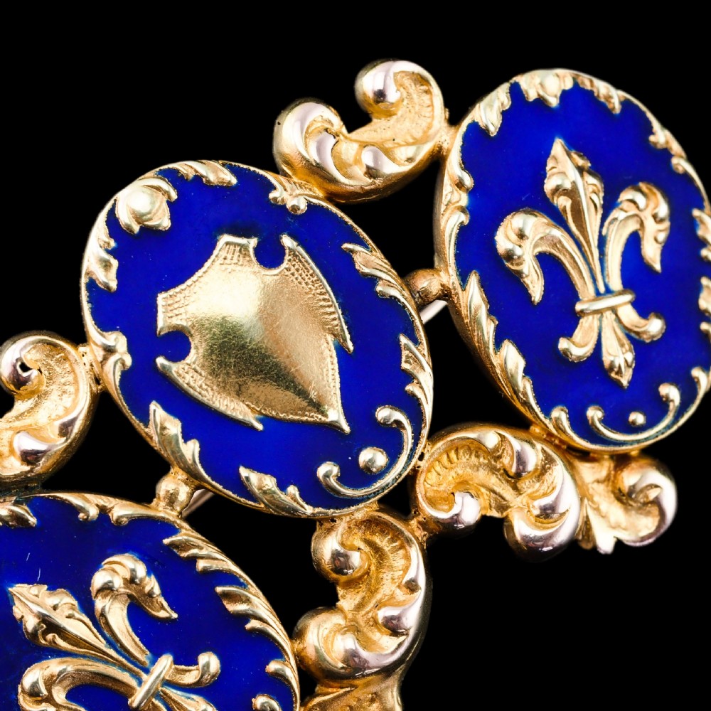 A 19th-century 18ct gold brooch featuring three dark blue enamel oval cartouches decorated with gold heraldic motifs and rococo scrollwork. View II