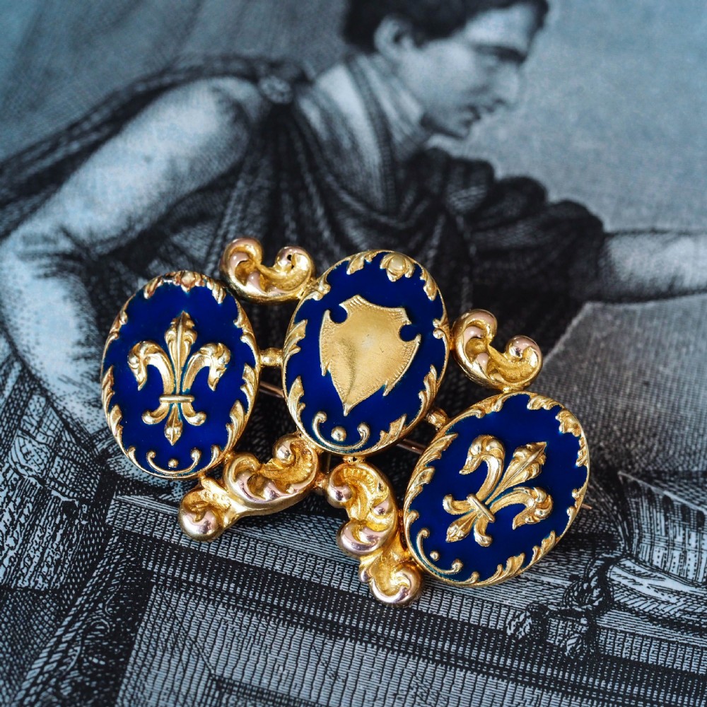 A 19th-century 18ct gold brooch featuring three dark blue enamel oval cartouches decorated with gold heraldic motifs and rococo scrollwork. View IV