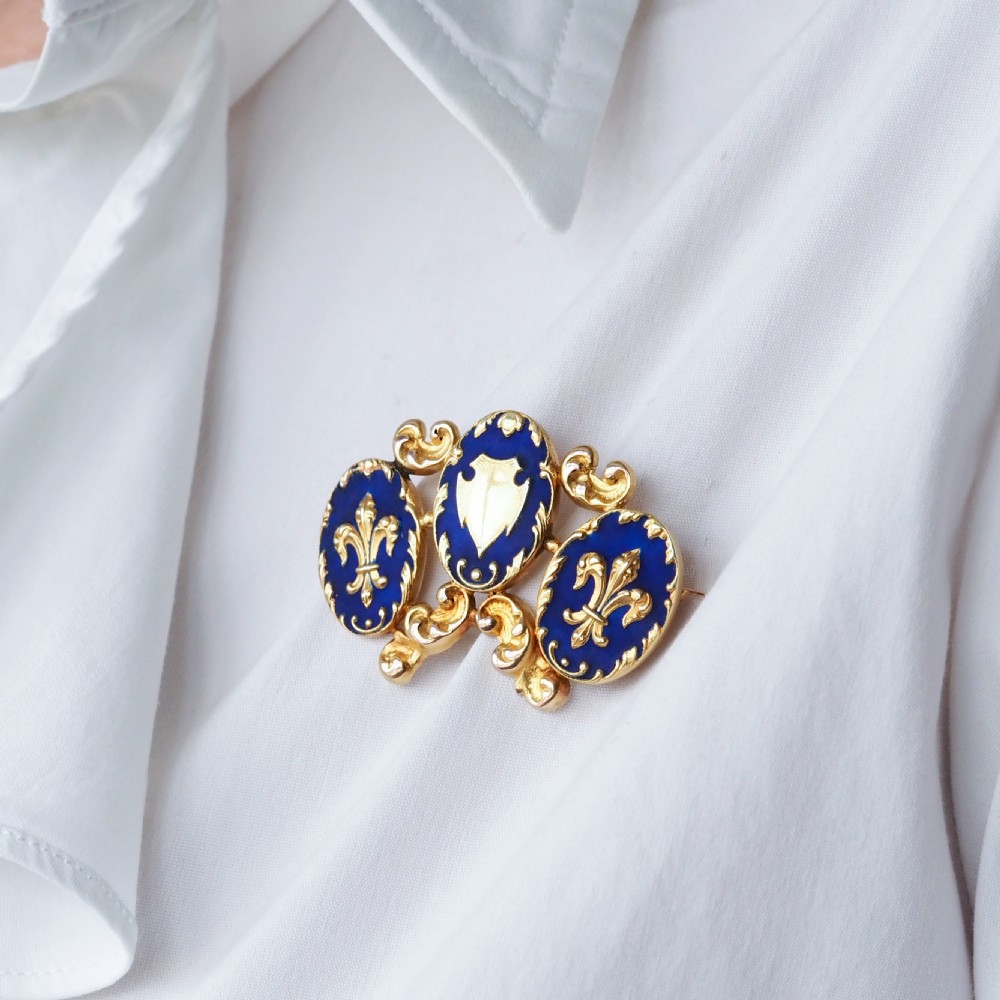 A 19th-century 18ct gold brooch featuring three dark blue enamel oval cartouches decorated with gold heraldic motifs and rococo scrollwork. View VII