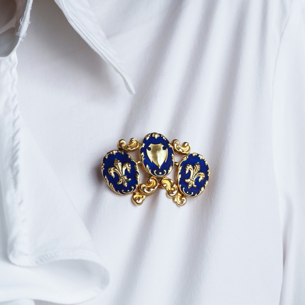 A 19th-century 18ct gold brooch featuring three dark blue enamel oval cartouches decorated with gold heraldic motifs and rococo scrollwork. View IX