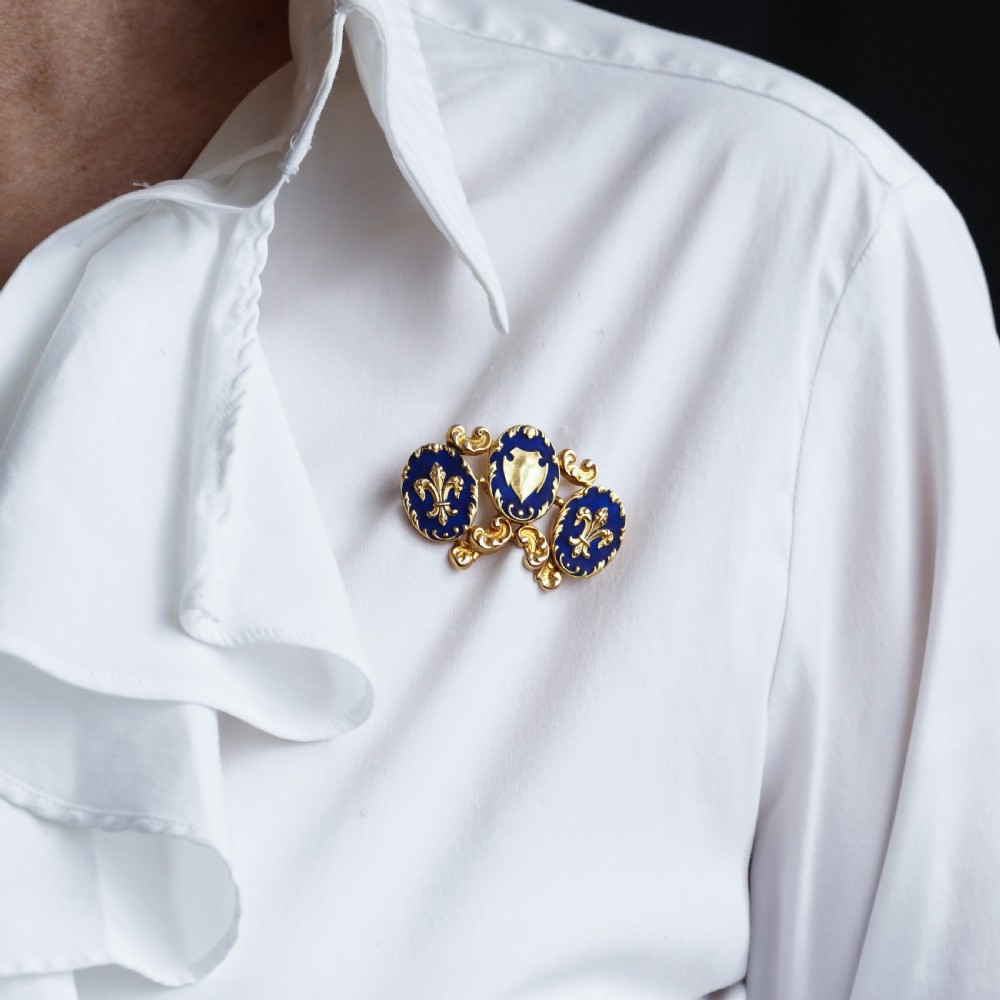 A 19th-century 18ct gold brooch featuring three dark blue enamel oval cartouches decorated with gold heraldic motifs and rococo scrollwork. View XI