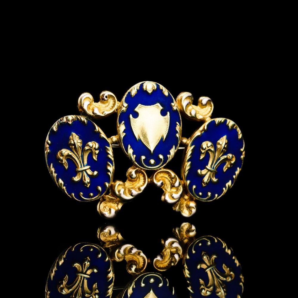 A 19th-century 18ct gold brooch featuring three dark blue enamel oval cartouches decorated with gold heraldic motifs and rococo scrollwork. View XII
