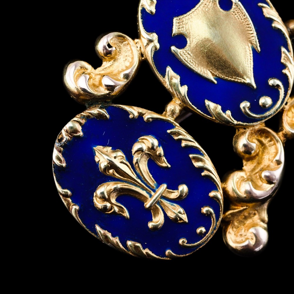 A 19th-century 18ct gold brooch featuring three dark blue enamel oval cartouches decorated with gold heraldic motifs and rococo scrollwork. View XIII