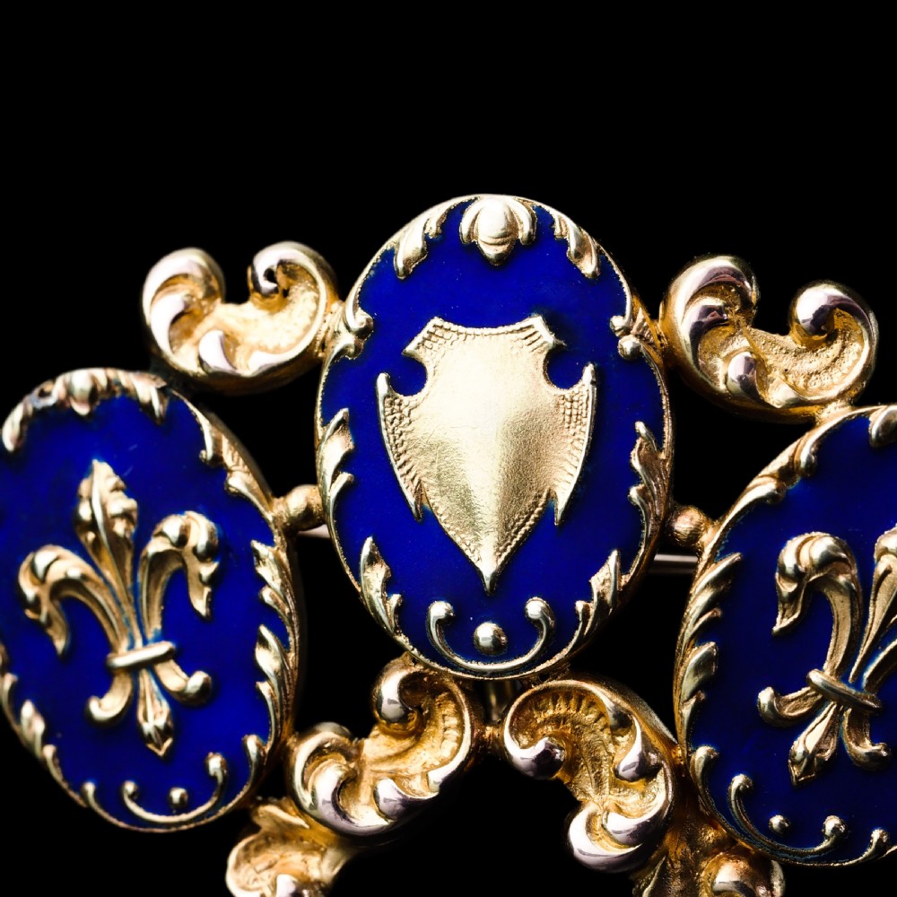 A 19th-century 18ct gold brooch featuring three dark blue enamel oval cartouches decorated with gold heraldic motifs and rococo scrollwork. View XIV