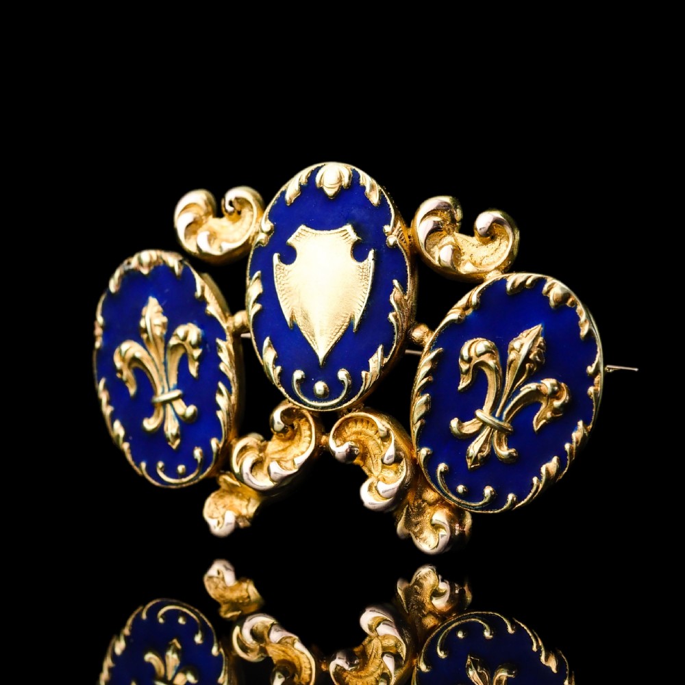 A 19th-century 18ct gold brooch featuring three dark blue enamel oval cartouches decorated with gold heraldic motifs and rococo scrollwork. View XV