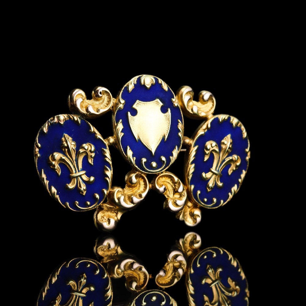 A 19th-century 18ct gold brooch featuring three dark blue enamel oval cartouches decorated with gold heraldic motifs and rococo scrollwork. View XVI