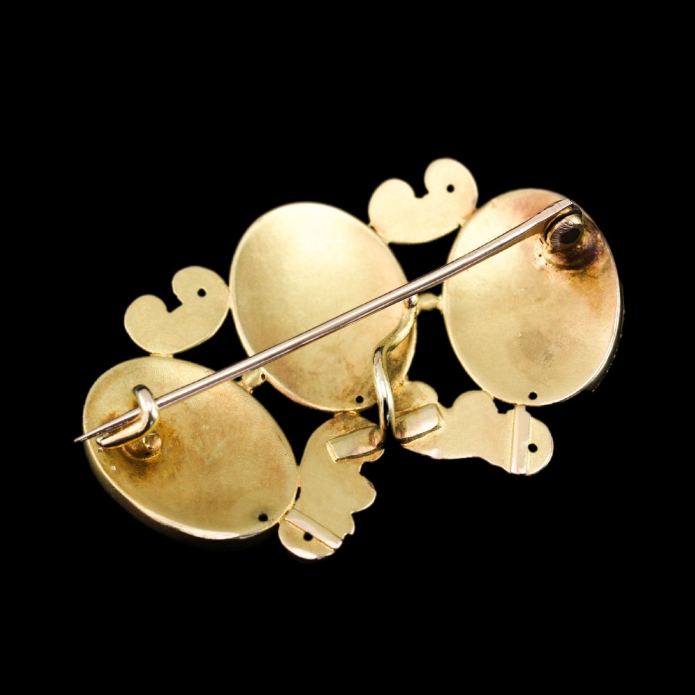 A 19th-century 18ct gold brooch featuring three dark blue enamel oval cartouches decorated with gold heraldic motifs and rococo scrollwork. View XVII