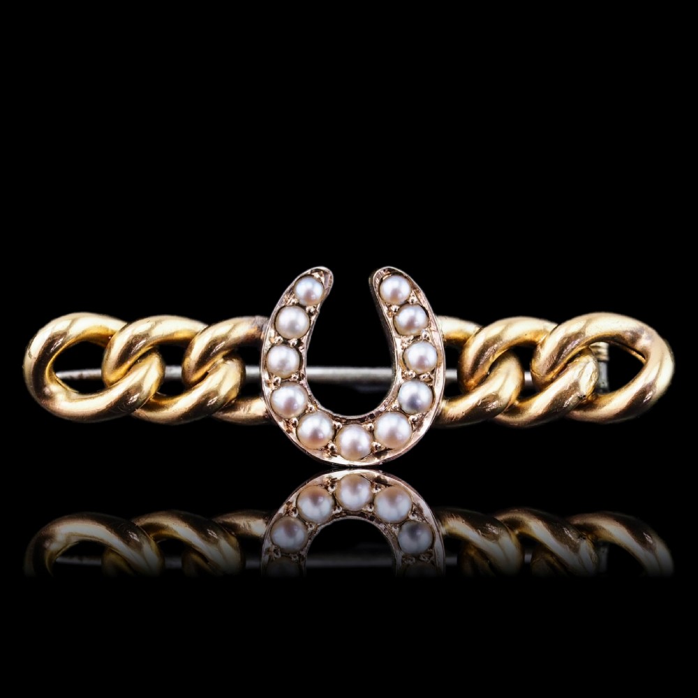An antique 15ct gold bar brooch featuring a central horseshoe motif set with seed pearls over a curb link design.
