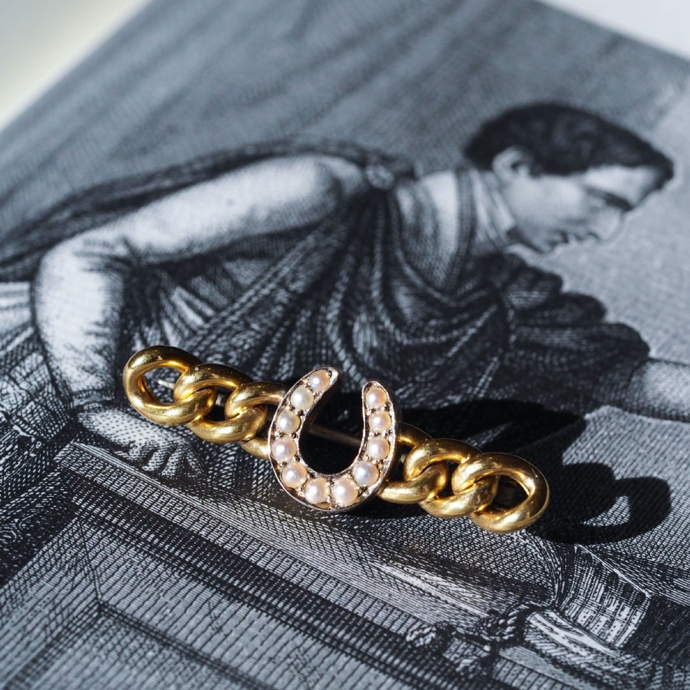 An antique 15ct gold bar brooch featuring a central horseshoe motif set with seed pearls over a curb link design. View VIII