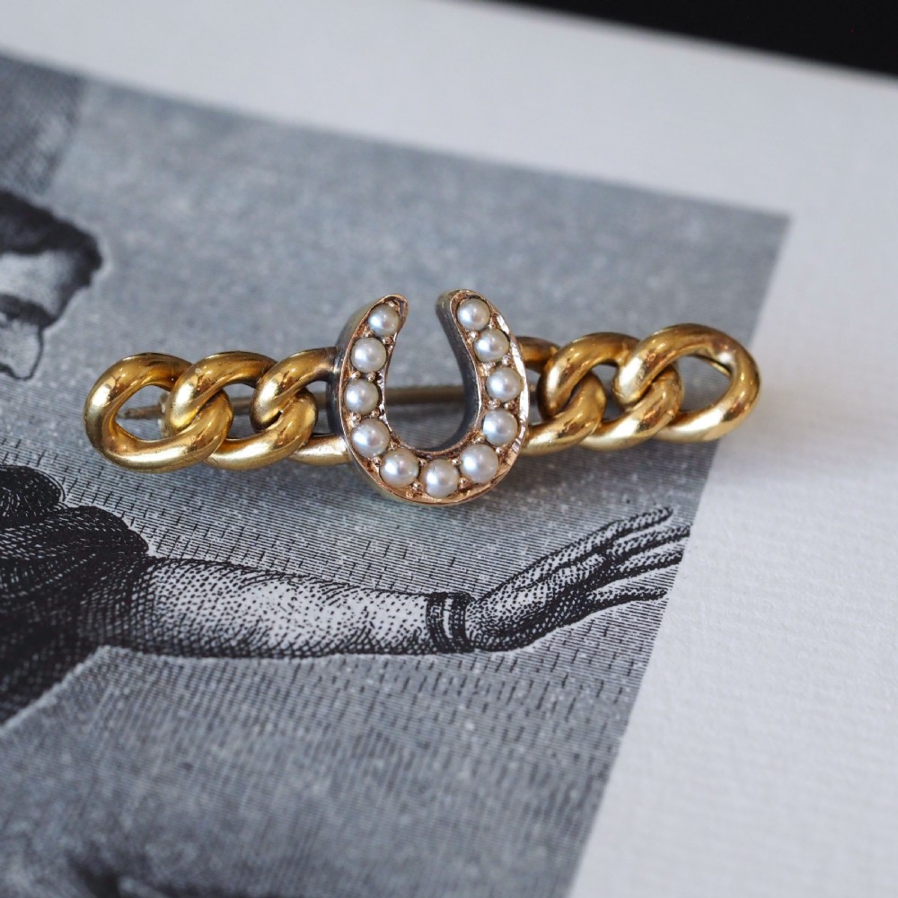 An antique 15ct gold bar brooch featuring a central horseshoe motif set with seed pearls over a curb link design. View X