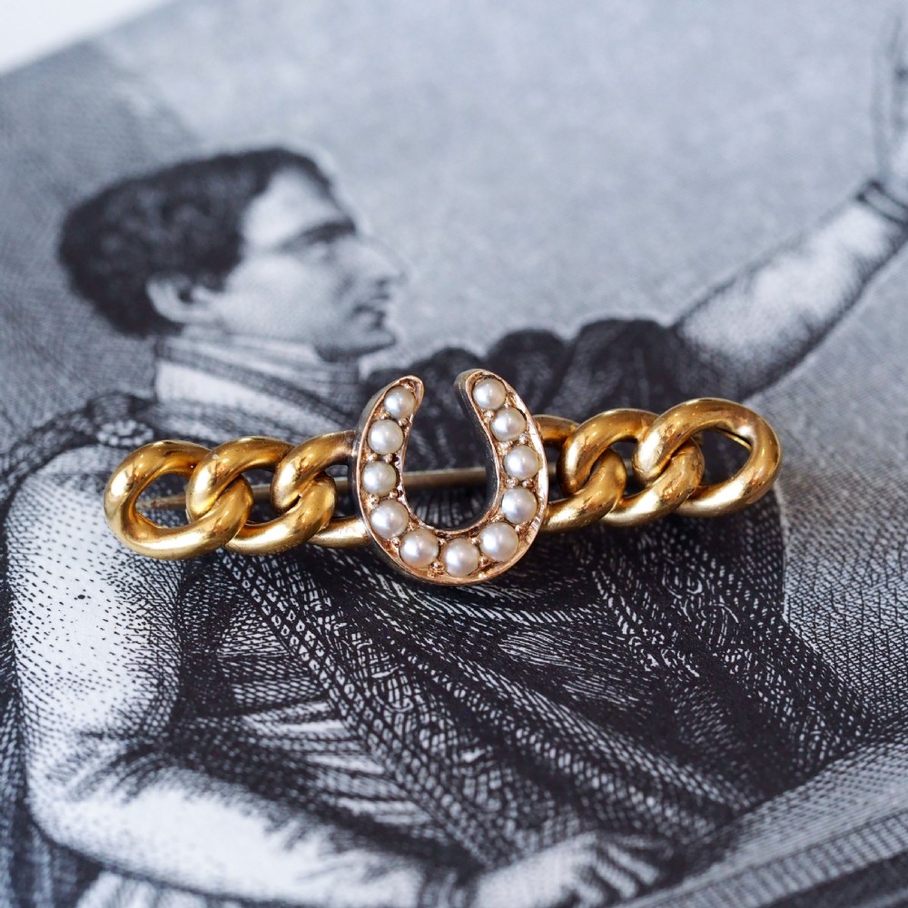 An antique 15ct gold bar brooch featuring a central horseshoe motif set with seed pearls over a curb link design. View XI