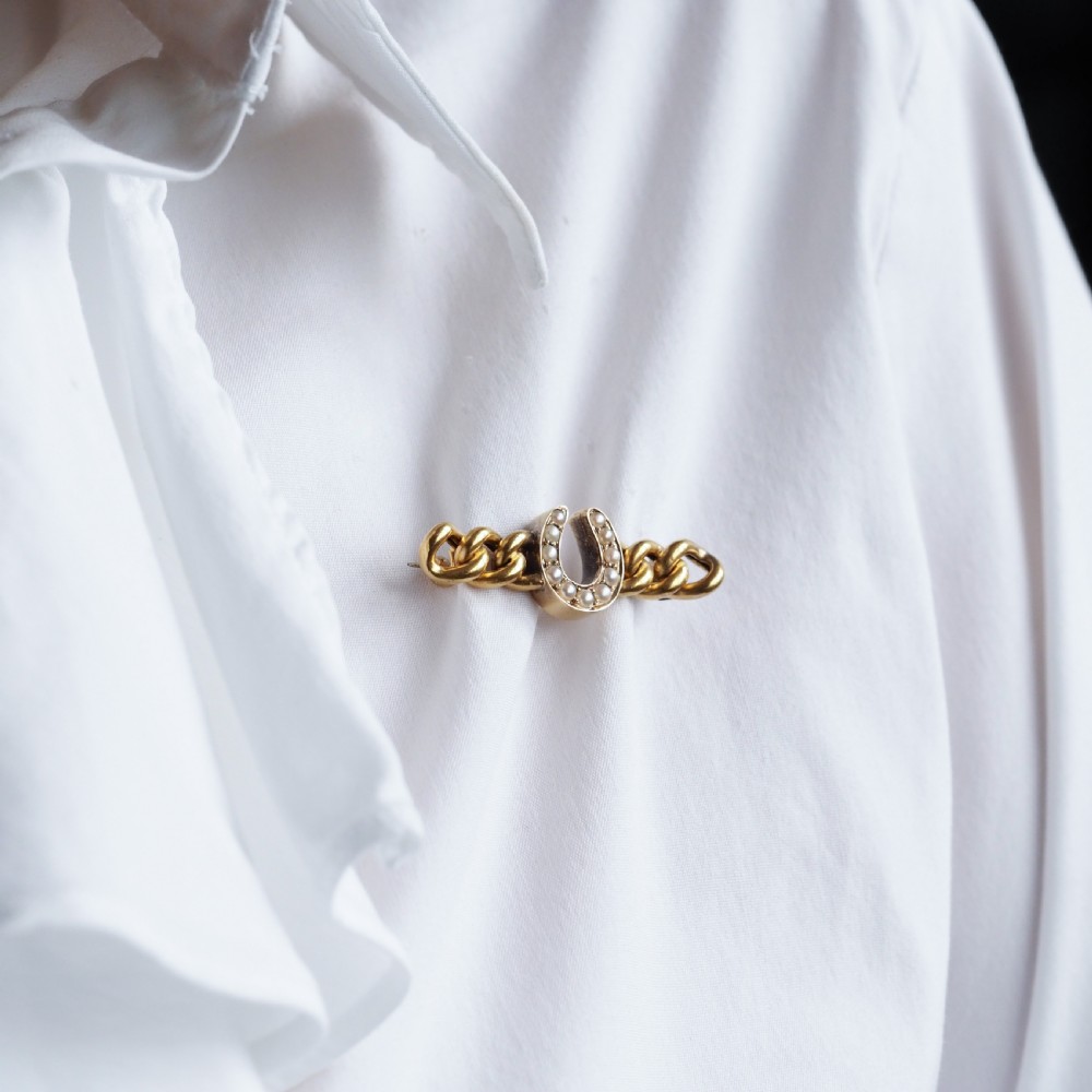 An antique 15ct gold bar brooch featuring a central horseshoe motif set with seed pearls over a curb link design. View XV