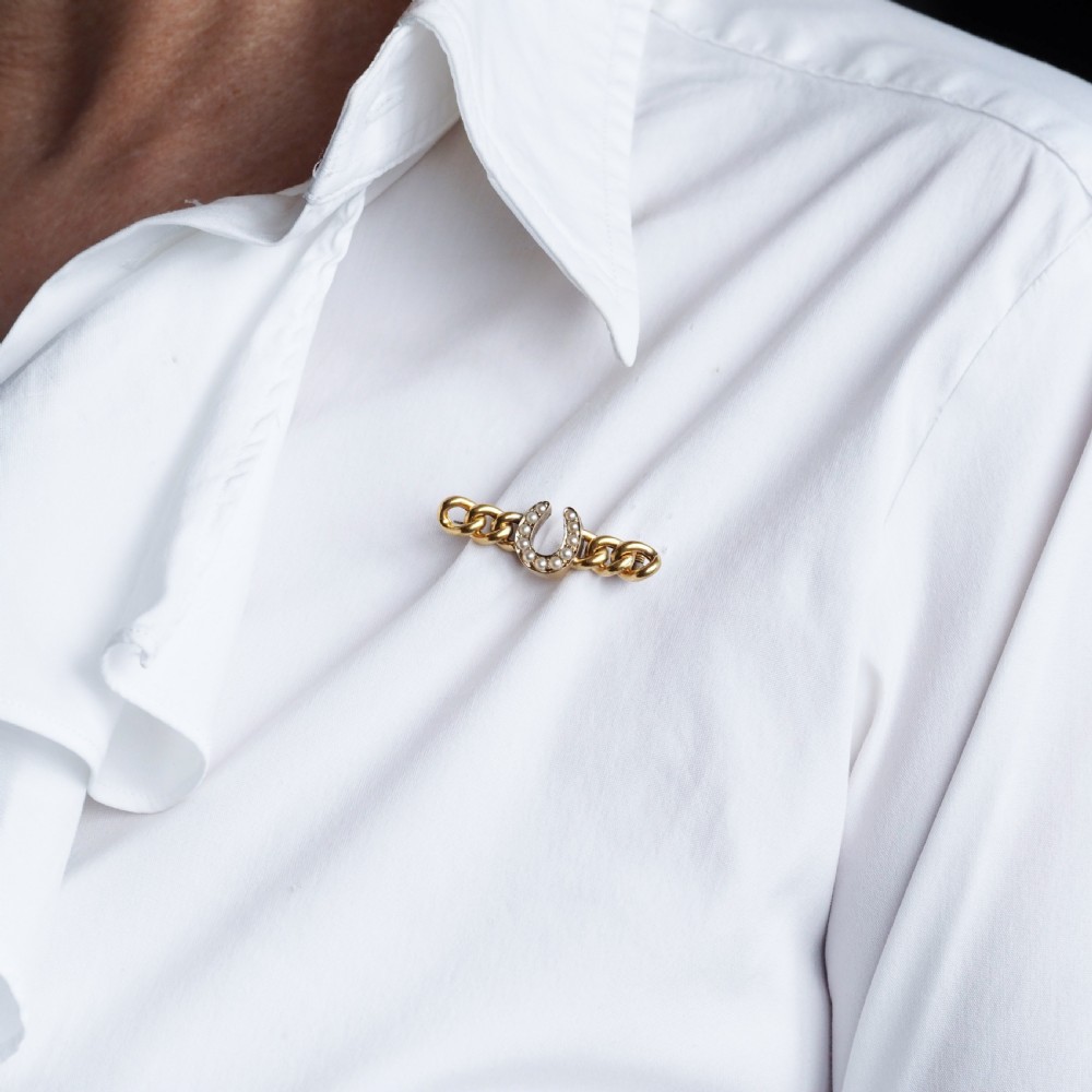 An antique 15ct gold bar brooch featuring a central horseshoe motif set with seed pearls over a curb link design. View XVI