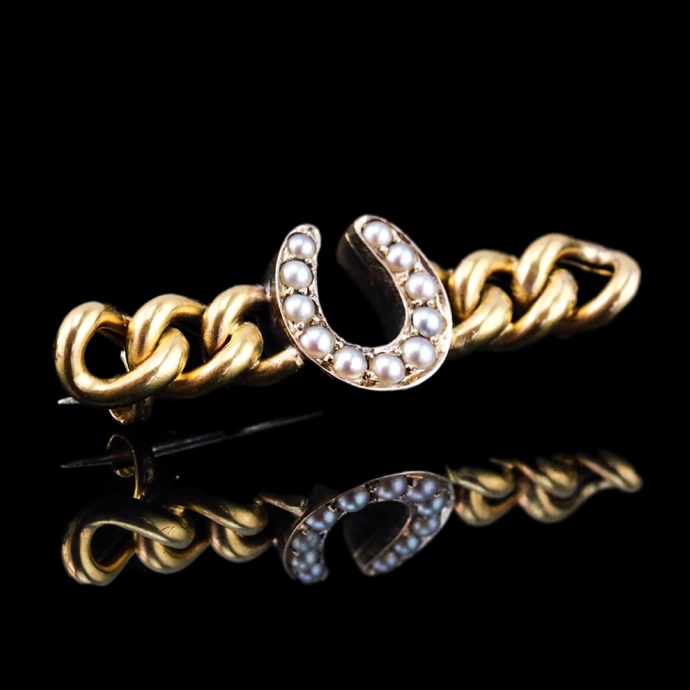 An antique 15ct gold bar brooch featuring a central horseshoe motif set with seed pearls over a curb link design. View XVIII