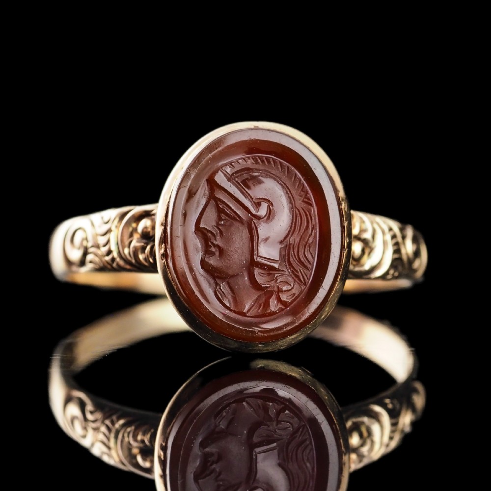 A Georgian gold ring featuring an oval reddish-brown carnelian stone engraved with the profile profile of a helmeted Roman soldier.