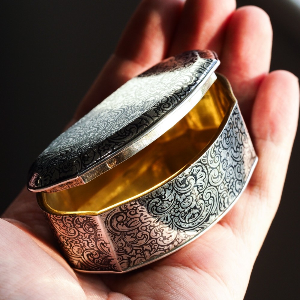 An antique French solid silver snuff box with black niello scrollwork engraving and a gilded gold interior.