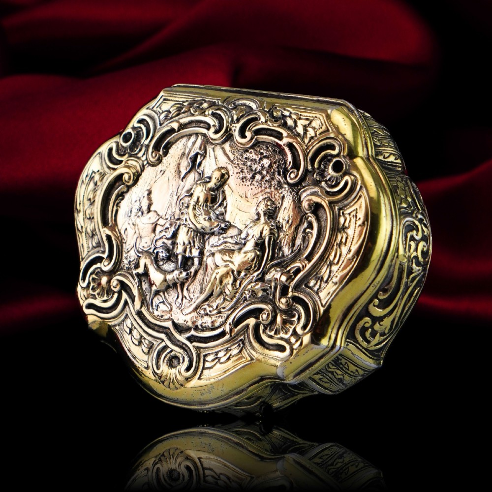 An eighteenth-century shaped oval silver-gilt table snuff box featuring Rococo scrollwork and a raised mythological scene on the hinged lid. View II