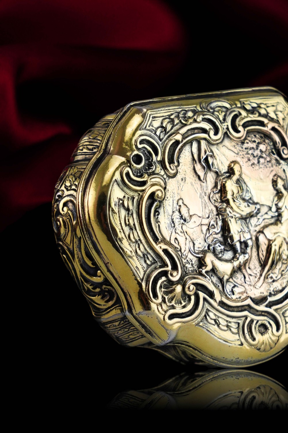 An eighteenth-century shaped oval silver-gilt table snuff box featuring Rococo scrollwork and a raised mythological scene on the hinged lid. View IV