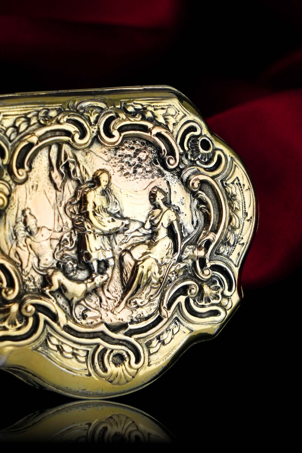 An eighteenth-century shaped oval silver-gilt table snuff box featuring Rococo scrollwork and a raised mythological scene on the hinged lid. View V