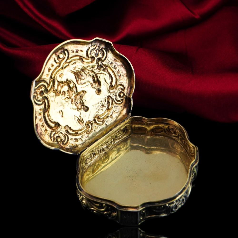 An eighteenth-century shaped oval silver-gilt table snuff box featuring Rococo scrollwork and a raised mythological scene on the hinged lid. View VIII